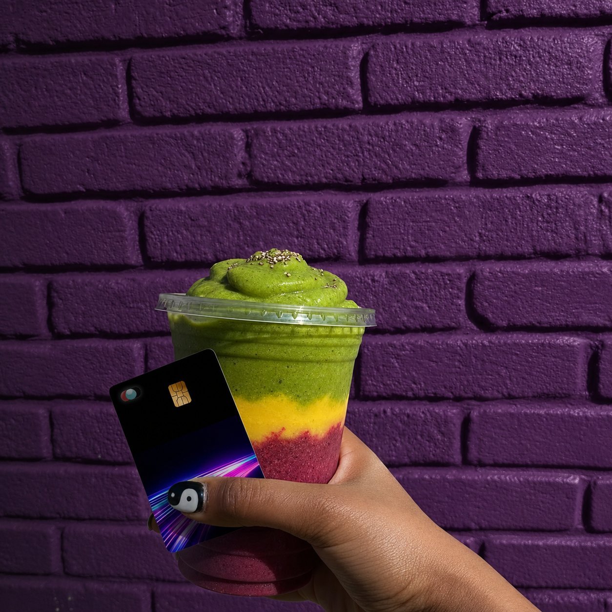 A hand holding a Blink card next to a layered smoothie against a purple brick wall